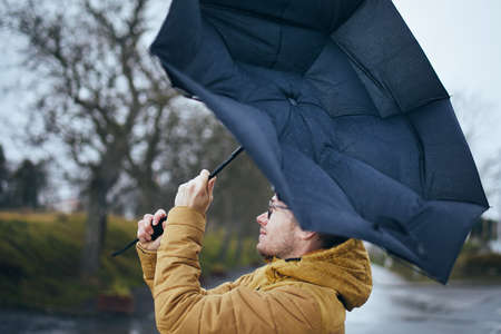 Man holding broken umbrella in strong wind during gloomy rainy day. Themes weather and meteorogy.の写真素材