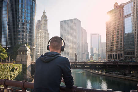 Rear view of pensive man with wireless headphones during city walk. Chicago cityscape, United States.の写真素材