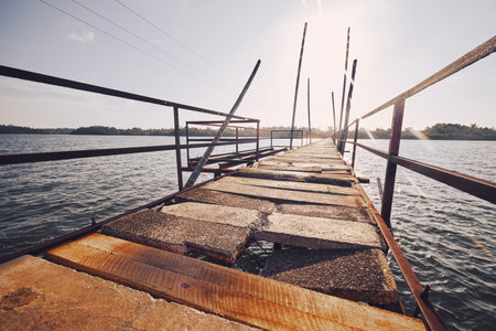 Old damaged bridge over water of lake on sunny day.の写真素材