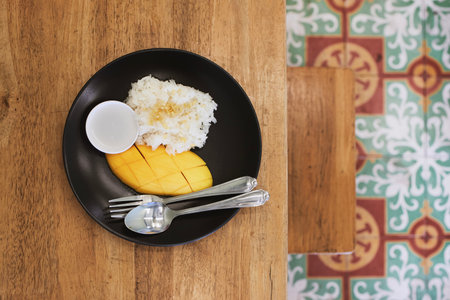Fresh mango with sticky rice and sweetened coconut milk on wooden table. Popular Thai food prepared on plate to eat.の写真素材