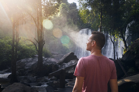 Man walking through rainforest to high waterfall in mountains. Tourist enjoying tropical nature in Camobodia.の写真素材