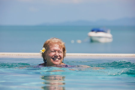 Active laughing senior woman in pool against sea. Woman is enjoying swimming during sunny day.の写真素材