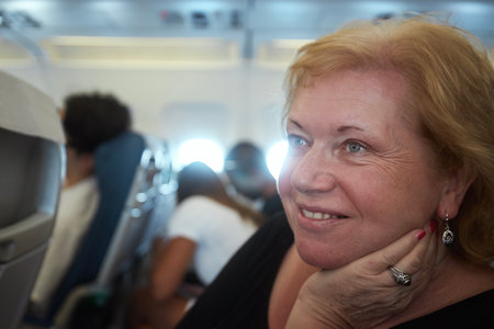 Portrait of senior woman with dreamy look while traveling by airplane. Passengers in airplane cabin during flight.の写真素材