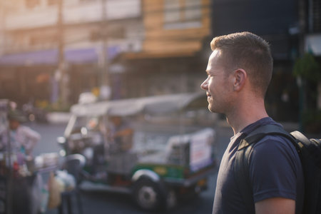 Portrait of tourist with backpack walking at street. Side view of man against tuk tuk on road. Bangkok, Thailandの写真素材