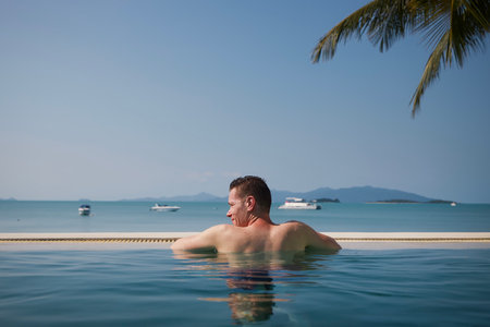 Rear view man while relaxing in swimming pool against sea with islands. Vacation on beach in tropical destination.の写真素材