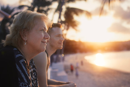 Portrait of senior woman with her adult son together looking at sand beach and sea at beautiful sunset.の写真素材