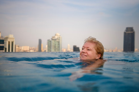 Active senior woman is swimming in pool with view towards modern city.の写真素材