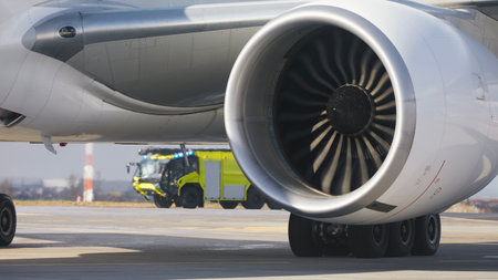 Fire truck of airport rescue and fire brigade behind engine of airplane on runway. Themes emergency and help in aviation.の写真素材