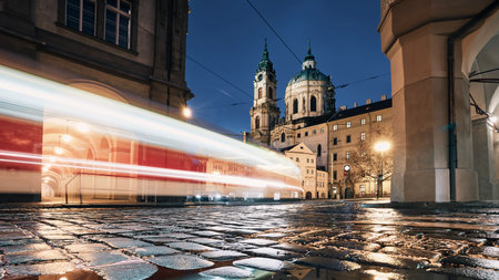 Light trail of tram passing between historical buildings at night. Wet cobblestones in Lesser Town in Prague, Czech Republic.の写真素材