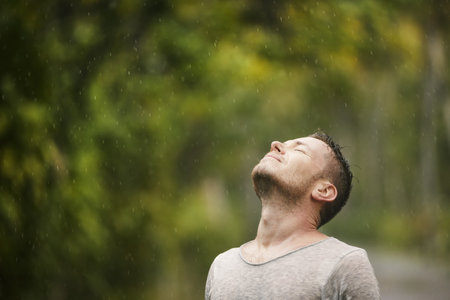 Portrait of man in wet clothes with eyes closed enjoying heavy rain in nature. Themes of life water, weather and environment.の写真素材