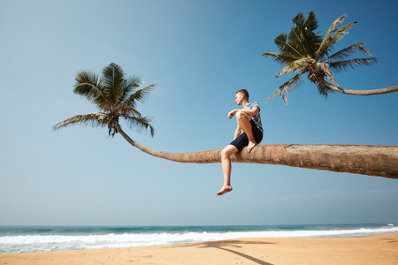 Man sitting on trunk of palm tree and enjoying sea view. Idyliic sand beach in Sri Lanka.の写真素材