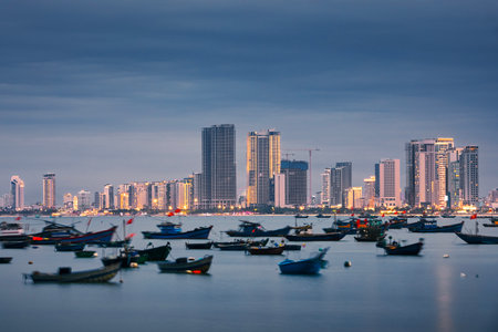 Da Nang cityscape at twilight. Fishing boat moored in port against illuminated coast with modern buildings.の写真素材