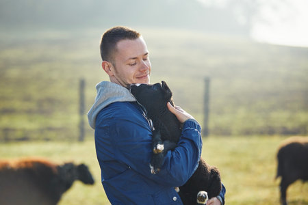 Man holding lamb in herd of sheep. Portrait of farmer in organic farm in countryside. Themes sustainable agriculture, ecology and animal care.の写真素材