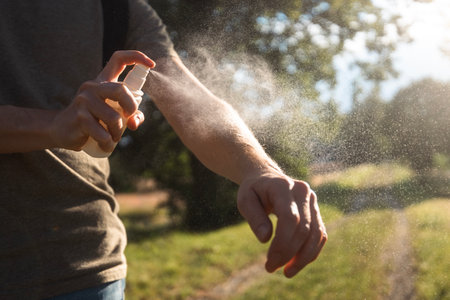 Prevention against mosquito bite during sunny summer day. Man is applying insect repellent on his...