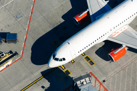Aerial view of white plane at airport. Airplane in front of passenger boarding bridge from terminal.
