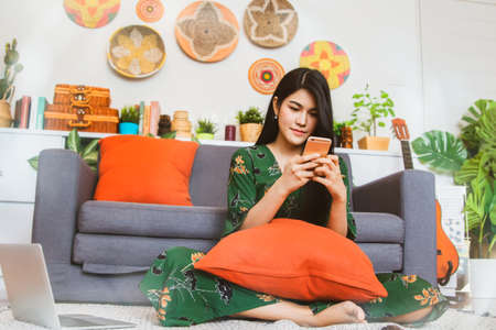 Asian woman with long hair wearing a green dress using a smartphone to search for a contact number...