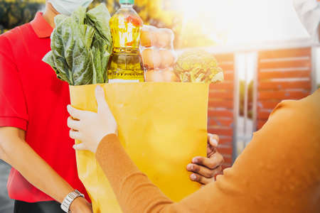 Concept ordering products from home : Red uniform male staff sent freshly cooked food packed in paper bags to female customers at home according to customer needs. Online delivery service with qualityの写真素材