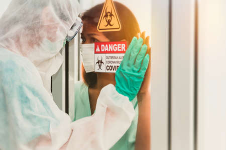 Concerns between infected women Coronavirus (Covid-19)and the young man wearing PPE protective clothing. Looking through the glass together in the containment room and closely monitoring the treatmentの写真素材
