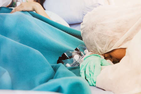Female doctor responsible for taking care of influenza patients, fatigue, hard work, drowsiness beside the patient and removing the plastic mask, sleep, care for female patients 24 hours.の写真素材
