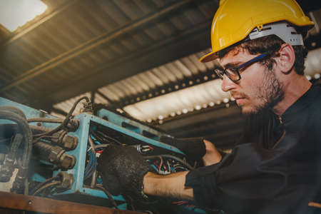 Male electrician in the factory is on duty to inspect the mechanical 3-phase electrical box of the machine and fix the damaged electrical connector with caution.の写真素材