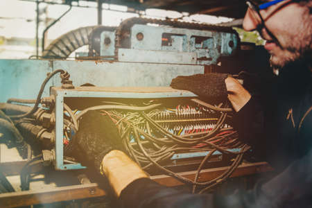 The male electrician in the factory has the duty to inspect the 3-phase electrical cable box of the disorderly machinery with the intention of and add caution for safety.の写真素材