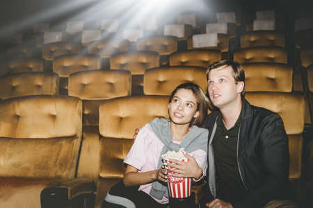 Couples, romantic at the cinema : Handsome and beautiful young women sit and watch the entertainment in the movie theater with pleasure, sitting and eating popcorn for more enjoyment.の写真素材