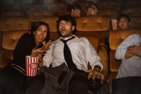 The couple, whose faces were excited, were shocked and frightened while watching a horror movie in a cinema together with a group of spectators seated close to each other.の写真素材