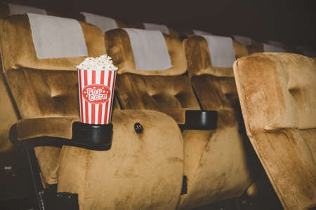 Popcorn is packed in a red paper cup placed on a chair in a movie theater eaten for added enjoyment.の写真素材