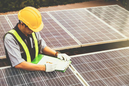 Male engineering workers wearing safety clothing work on the roof, recording data at each solar panel during installation to test the power and to collect operational data : Selective Focusの写真素材