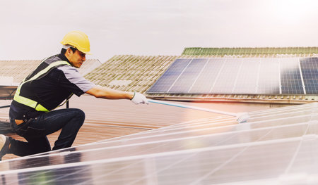 Side view Asian technicians cleaning blue outdoor solar photovoltaic panels to optimize functionality : Cleaning and inspection of solar panels on the roof of industrial plants : Selective focusの写真素材