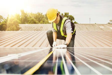 Solar panel installation work concept : Asian electrical engineer architects used a tape measure to measure the length of solar panels on the roof of an industrial factory.の写真素材