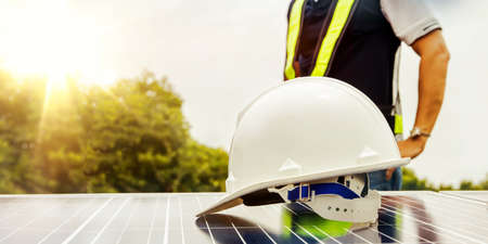 Male engineer works on the rooftop of an industrial factory building, conducts operations, controls the installation of solar cells, places white helmets on solar panels.の写真素材