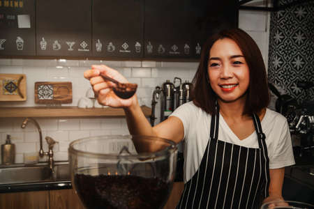 Portrait smiling Asian barista was happy to select Arabica coffee beans that were fragrant and put them into a coffee grinder to make quality coffee : Working women, coffee shop business ownersの写真素材