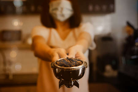 Young lady's barista delivers quality freshly roasted coffee in a luxurious coffee shop. Professional selection of coffee beans : Business woman or barista wearing a mask in a coffee shop holding portの写真素材