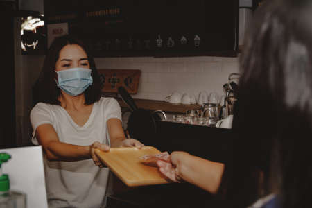 Female baristas who wear masks in food and beverage restaurants, provide cashless payments without contact with customers for safety during the global Coronavirus (Covid-19) outbreak.の写真素材