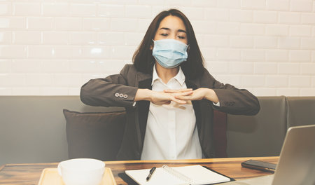 Middle-aged business woman who wears a mask, gets finger pain from business work in an office, is suffering from Office Syndrome on the wrist, she is having a kneading massage to relax.の写真素材
