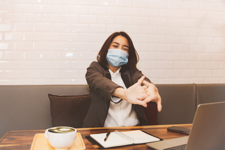 Middle-aged business woman wearing a mask, sitting on her wrists aching from business work in an office, has fatigue from office syndrome on her wrists, she feels uncomfortable.の写真素材