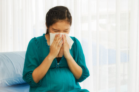 Pregnant women, unhealthy, causing complications of the common cold, and having allergies, sneezing on the patient's bed, using tissue to blow the fluid out of the nose for hospitalization.の写真素材