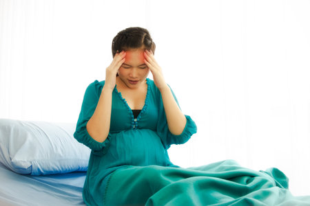 Asian pregnant women sit with migraine headaches with stress in patient beds, dizziness, headache: waiting for hospital treatmentの写真素材