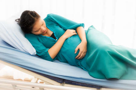 Pregnant Asian woman embraces her stomach and has pain in her stomach near giving birth : Young woman expected her child to be safe from the birth.の写真素材
