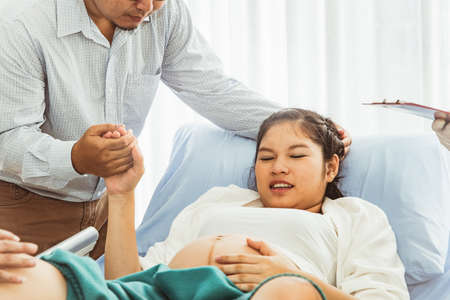 Taking care and holding hands Encouragement The pregnant wife is nearing the due date of birth, her husband is by her side without abandoning even the wife is very painful.の写真素材