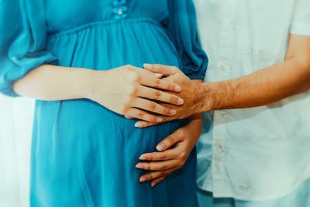 Wife's hand is placed on top of the husband's hand, sharing a gentle touch of the womb, a show of family love for the fetus.の写真素材