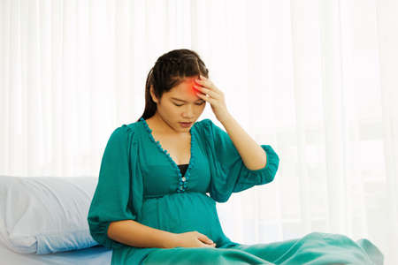 Asian pregnant woman. Headache on the left Migraine in the patient's bed, dizziness with pain due to stress. Sitting in the bed, the patient waiting for medical treatment in the hospitalの写真素材