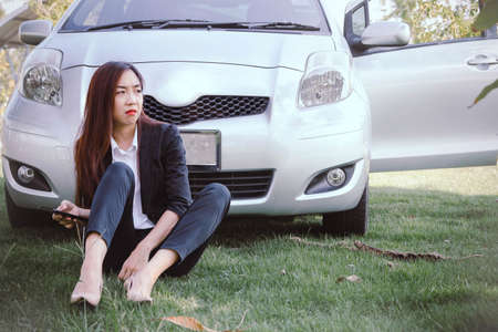 Businesswoman sitting in front of the car, parked on the grass in a place that was unfamiliar with facial expressions, and the eyes were worried because she was lost : Copy spaceの写真素材