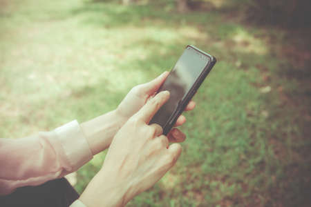 Smartphone Concept Everywhere, Woman uses her hand to touch the screen to search for messages or other information in the application while sitting on the green lawn.の写真素材