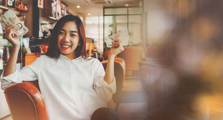 Portrait beautiful woman sitting in a coffee shop, showing a five thousand baht Thai banknote, along with the joy of spending cash on a daily basis : Copy Spaceの写真素材