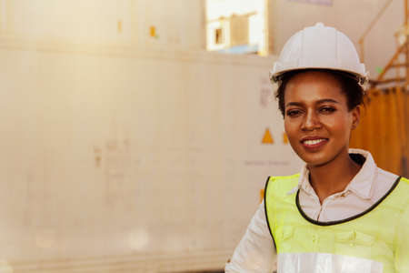 Happiness Portrait of an African-American female worker wearing a white safety helmet in a container warehouseの写真素材