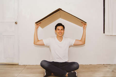 Portrait cheerful positive rejoicing handsome young man entered his new home and used cardboard as the roof of the house : Selective Focusの写真素材