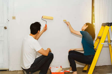Asian couple is using a water-based paint roller to prime the walls of their home for a simple interior decoration.の写真素材