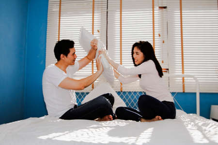 Couples have fun in bed, teasing and bullying with pillow fights in their bedroom at homの写真素材